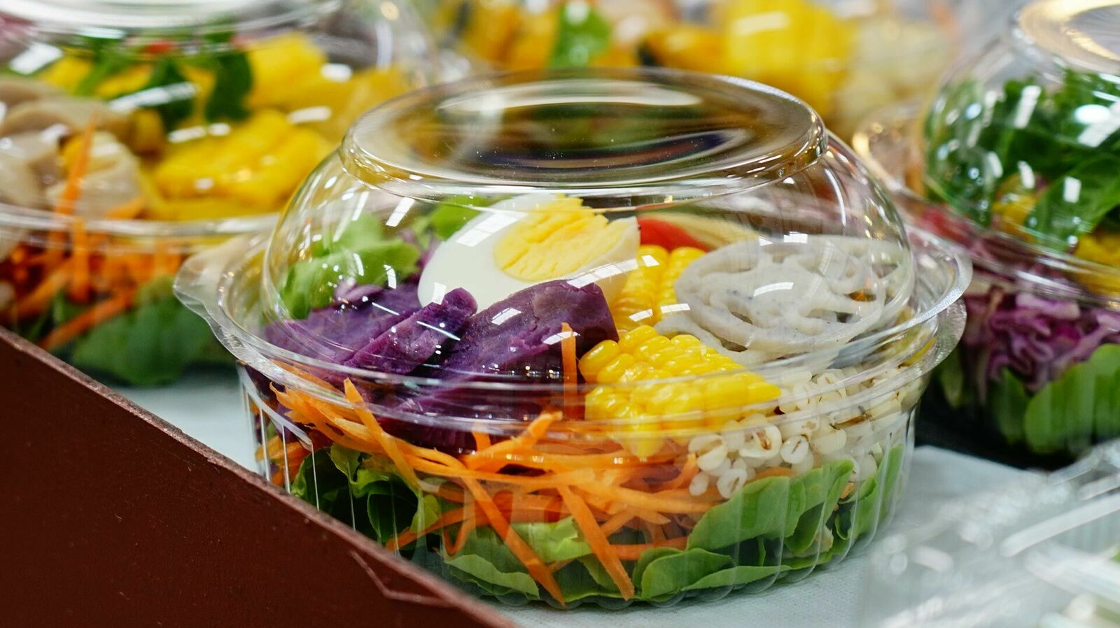 In einem Kühlregal stehen mehrere bunte Salate in einer durchsichtigen Kunststoff-Verpackung