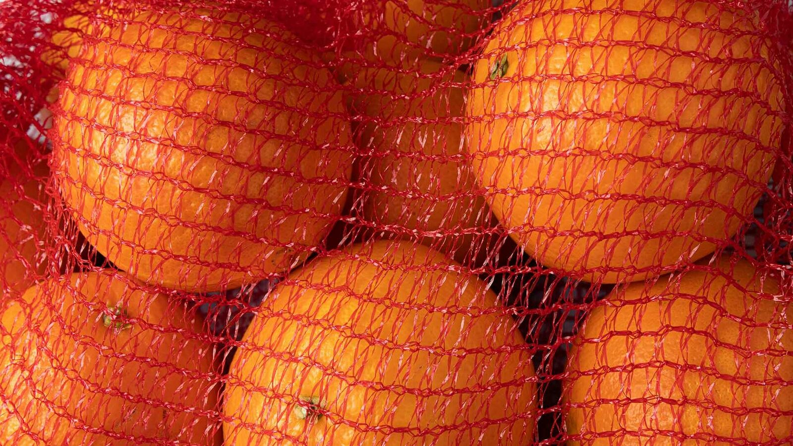 Nahaufnahme von einem roten Netz aus Kunststoff mit Orangen