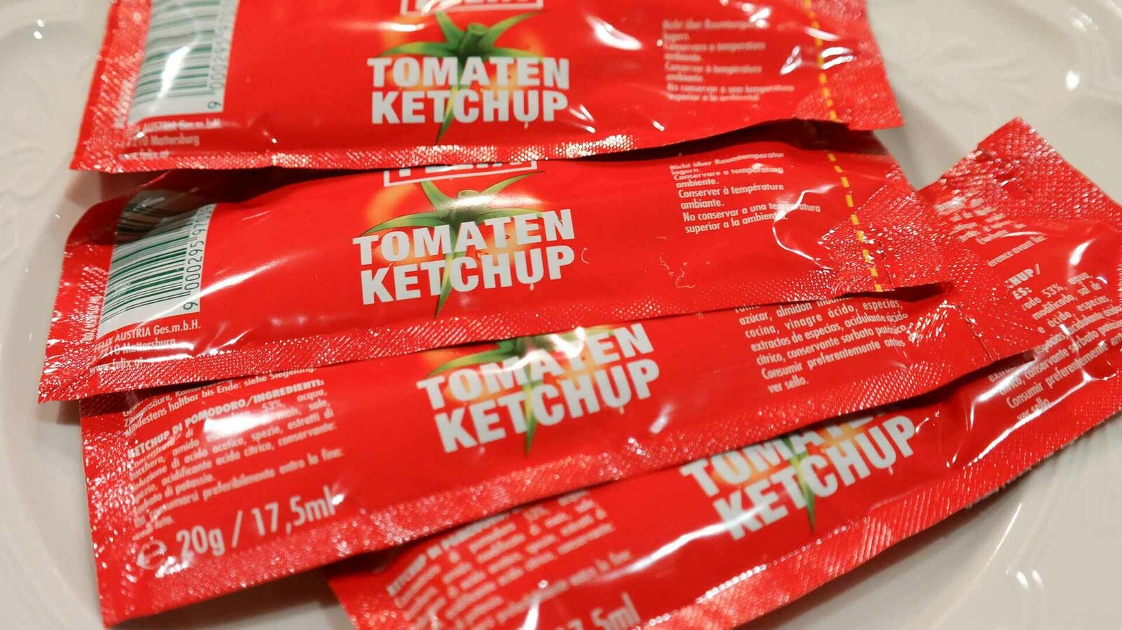 Auf einem weißen Teller liegen vier Einzelportionen Ketchup in Kunststoffverpackung