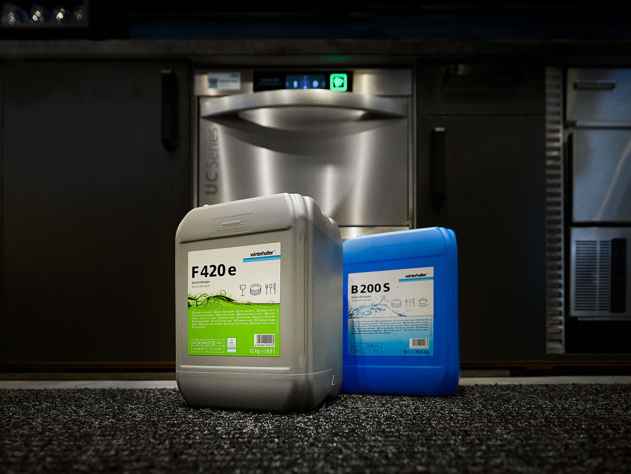 Conseils pour prévenir la corrosion du verre : utilisez des produits chimiques pour le lavage du verre Deux bidons contenant des produits lessiviels pour le lavage du verre et un dispositif de dosage à côté d'un lave verres comme protection contre la corrosion du verre