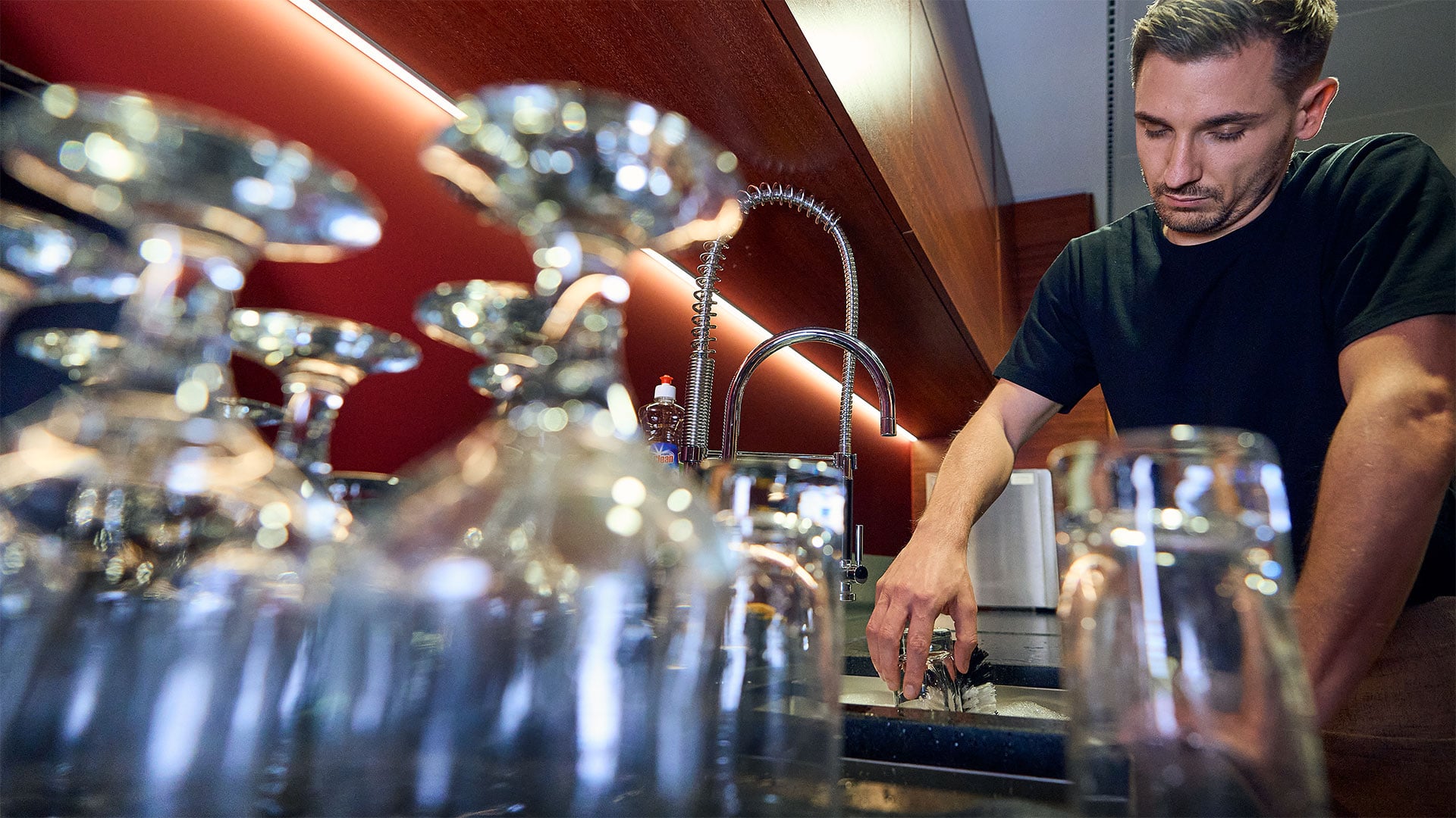 Inconvénient du lavage des verres à la main : chronophage et coûteux Un homme se tient devant l'évier d'un comptoir de bar et, épuisé, s'appuie d'un bras sur le bord de l'évier